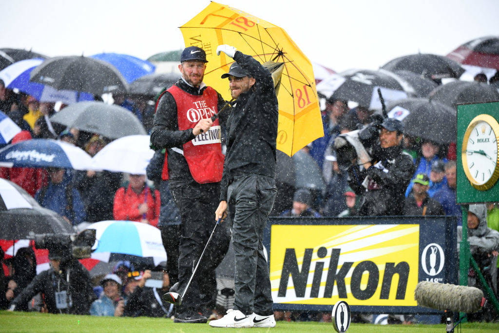 Tommy Fleetwood watches on under an umbrella